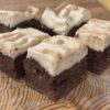 Vegan brownie cheesecake bars cut into squares and displayed on a rustic wooden cutting board, drizzled with a rich caramel sauce