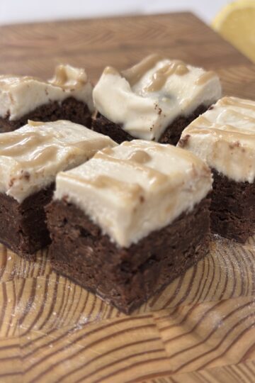 Vegan brownie cheesecake bars cut into squares and displayed on a rustic wooden cutting board, drizzled with a rich caramel sauce