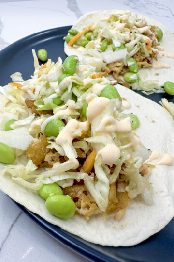 Two tacos filled with shredded tofu and vegetables, presented on a blue plate, showcasing a vibrant meal.