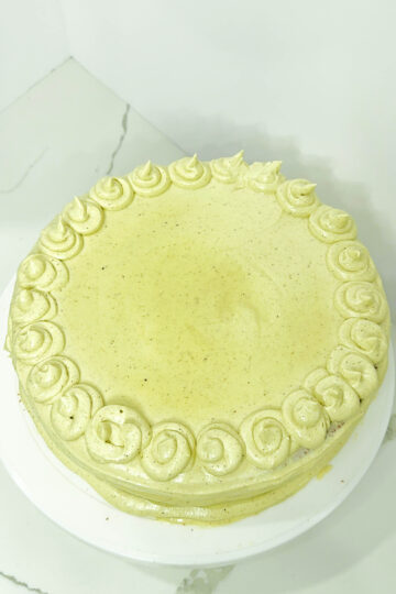 A beautifully decorated cake topped with vegan pistachio buttercream, elegantly presented on a white plate.