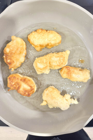 Crispy beer-battered tofu fillets frying in a pan, golden brown and bubbling in hot oil.