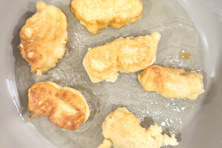 Crispy beer-battered tofu fillets frying in a pan, golden brown and bubbling in hot oil.