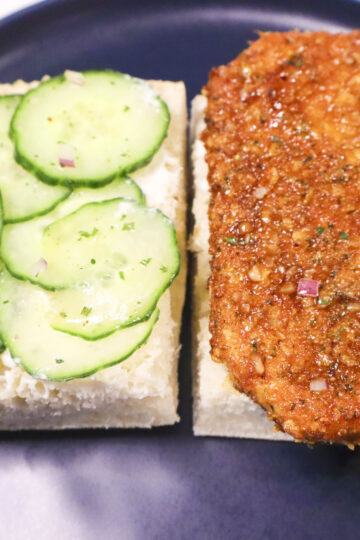 Open-face Vegan Cornflake "Chicken" Sandwich on a plate, showcasing crispy tofu with garlic butter sauce, creamy cashew spread, marinated cucumber, and red onion.