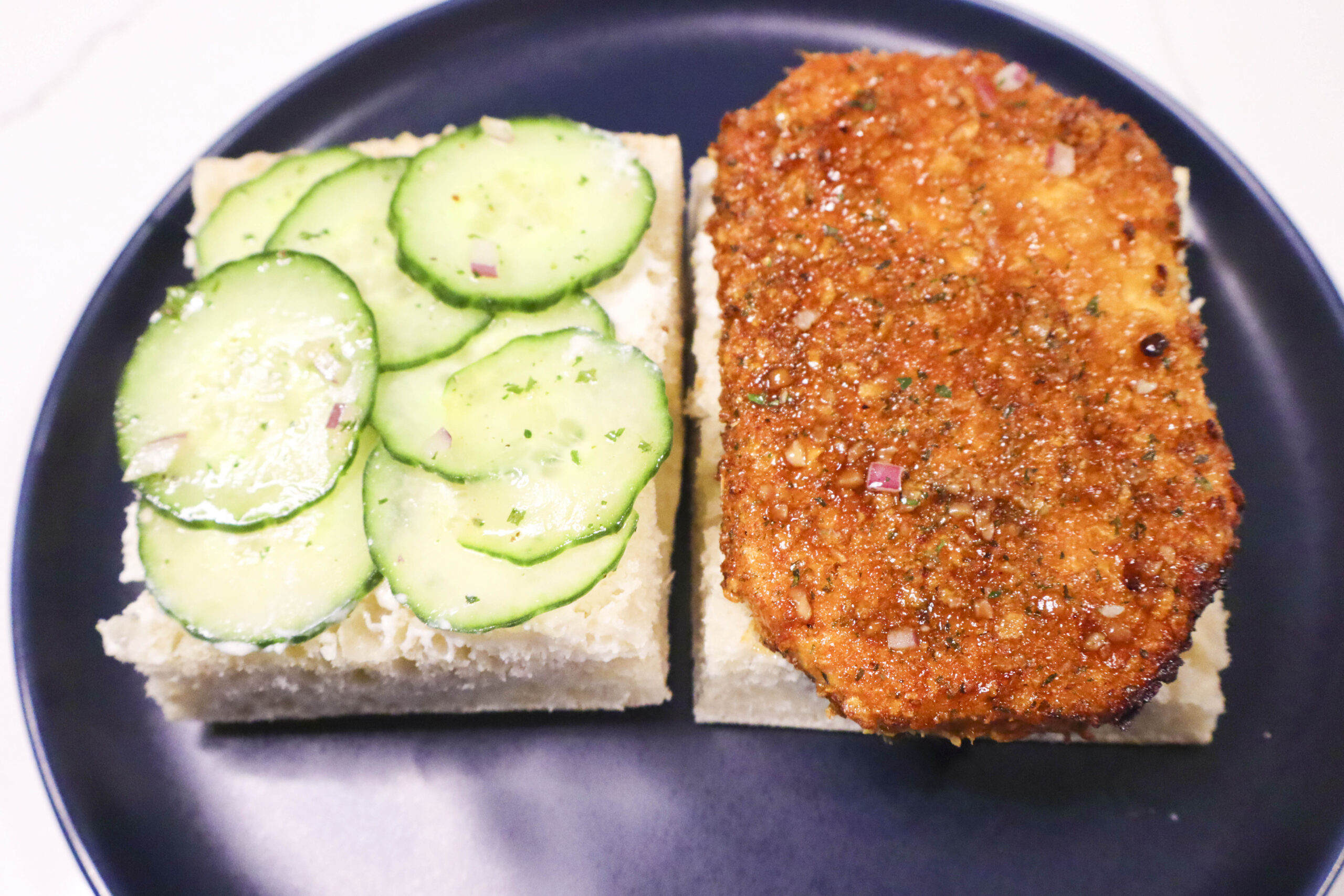 Open-face Vegan Cornflake "Chicken" Sandwich on a plate, showcasing crispy tofu with garlic butter sauce, creamy cashew spread, marinated cucumber, and red onion.