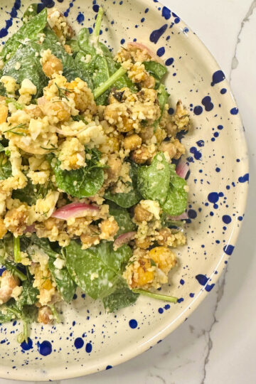 A vibrant bowl of roasted butternut squash and feta salad with chickpeas, couscous, fresh herbs, pickled onions, and a drizzle of creamy yogurt tahini dressing.