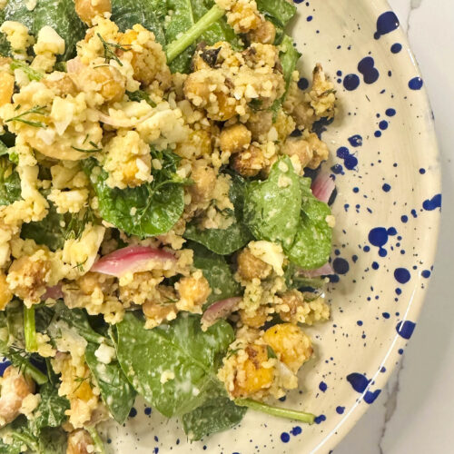 A vibrant bowl of roasted butternut squash and feta salad with chickpeas, couscous, fresh herbs, pickled onions, and a drizzle of creamy yogurt tahini dressing.