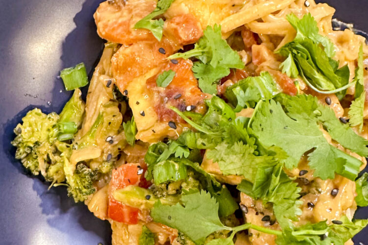 A vibrant vegan spicy peanut noodle bowl featuring broccoli and meat alternatives on a decorative plate.