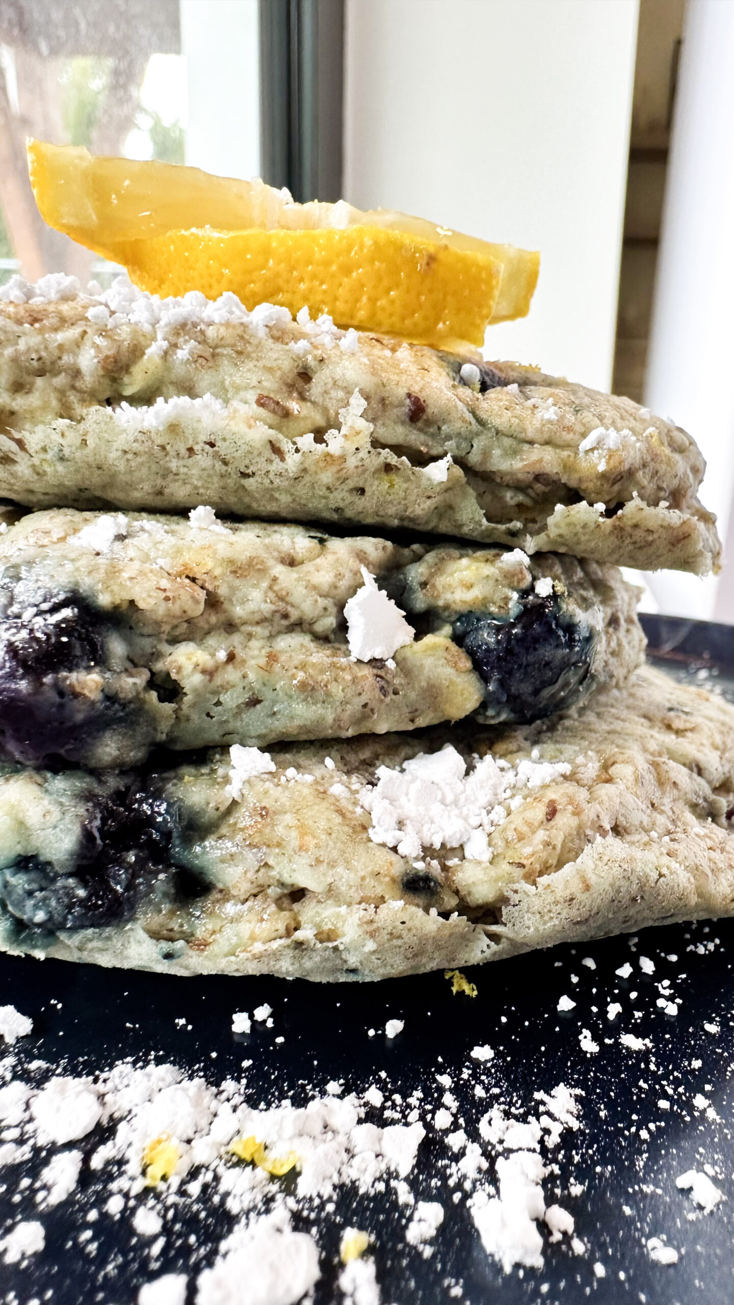 A stack of blueberry oatmeal pancakes topped with a lemon wedge, showcasing a delicious vegan breakfast option.