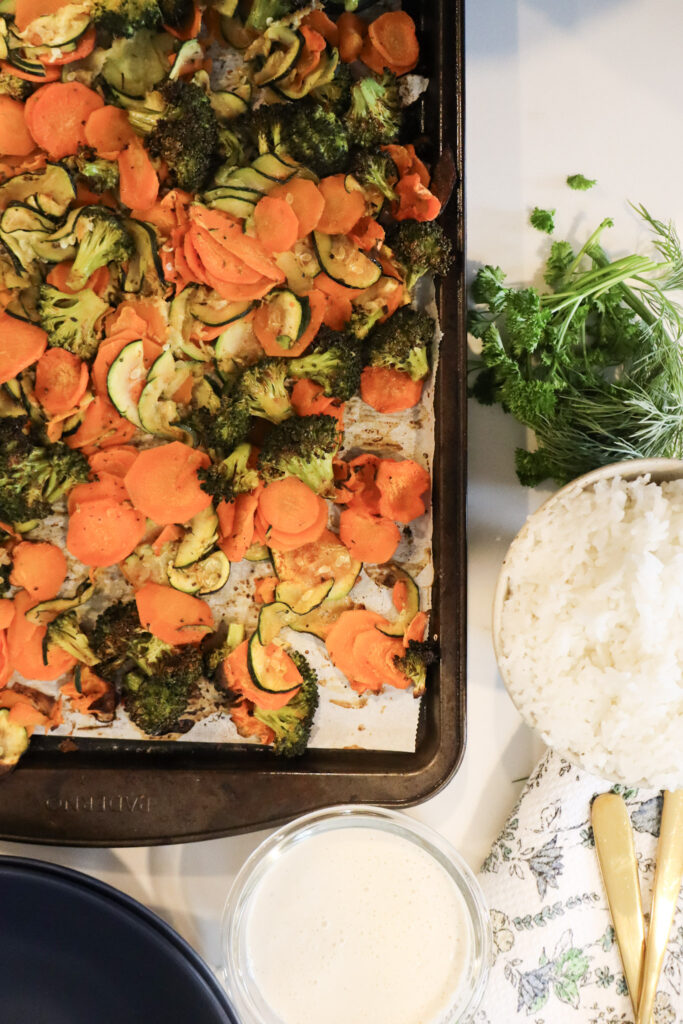A tray filled with fresh vegetables, prominently featuring vibrant orange carrots and green broccoli florets with rice and sauce on the side