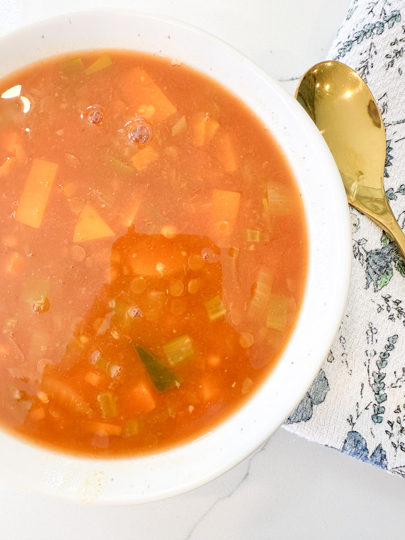 A bowl of vegetable soup in a white bowl with a gold spoon on the side
